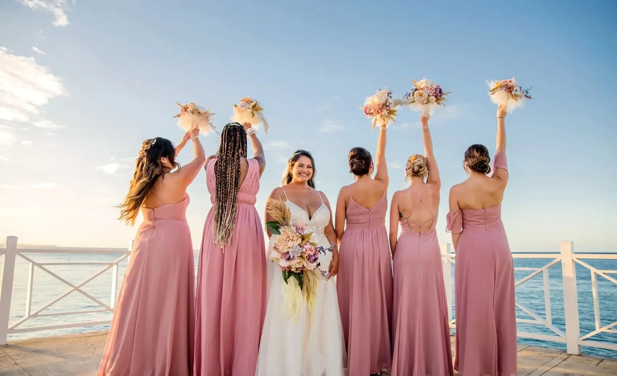 Bride and bridesmaids raising bouquets on a pier at Moon Palace Jamaica, Ocho Rios