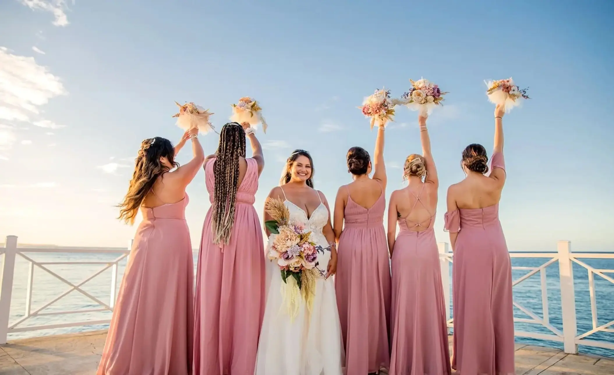Bride and bridesmaids raising bouquets on a pier at Moon Palace Jamaica, Ocho Rios