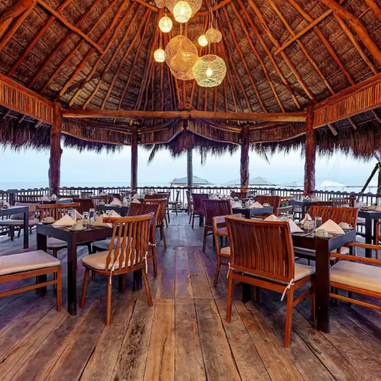 Open-air restaurant with a thatched palapa roof and wooden tables at Mystique Holbox, Isla Holbox