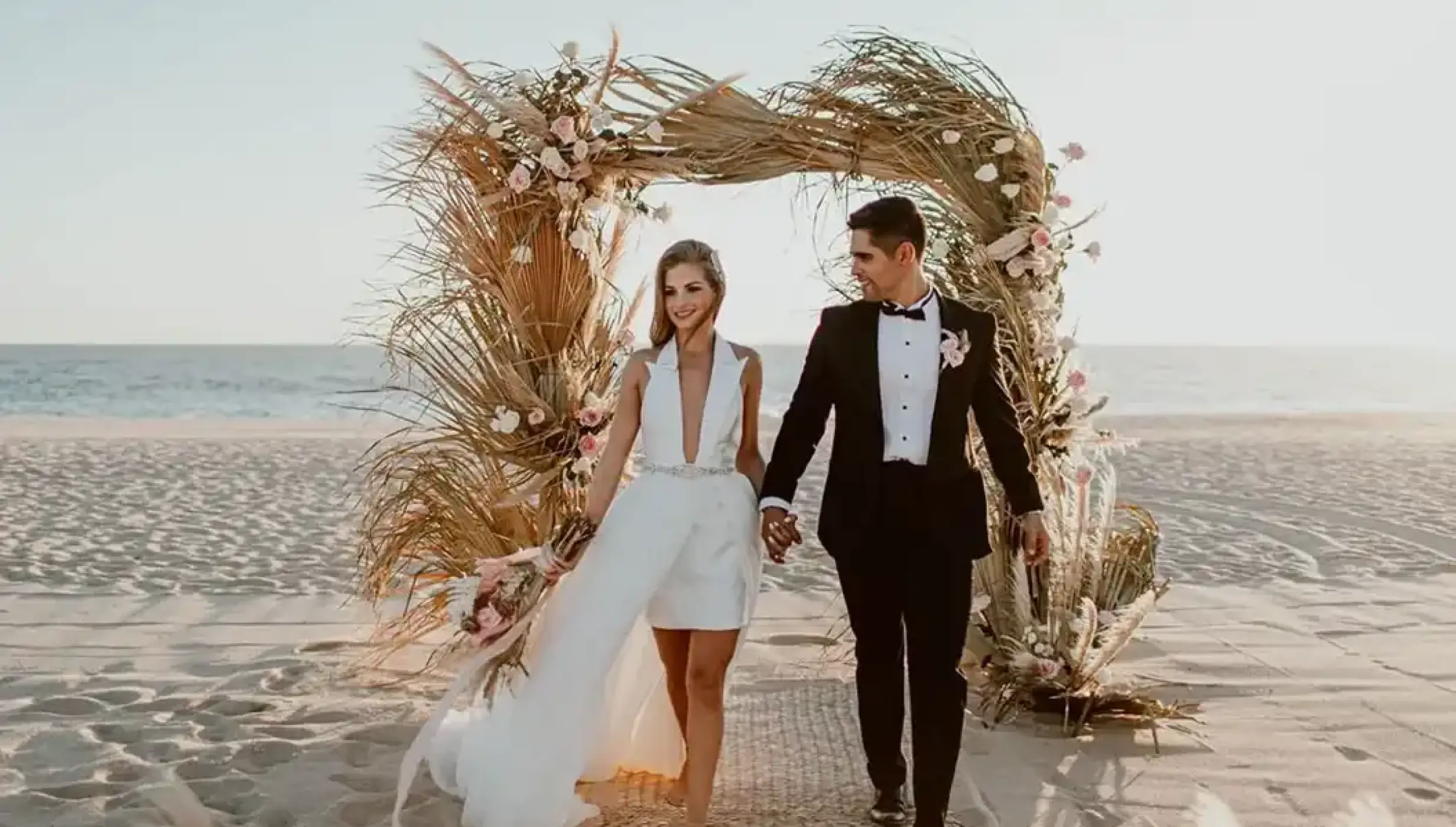 Bride and groom walking through a pampas grass archway at Nobu Hotel Los Cabos, Cabo San Lucas