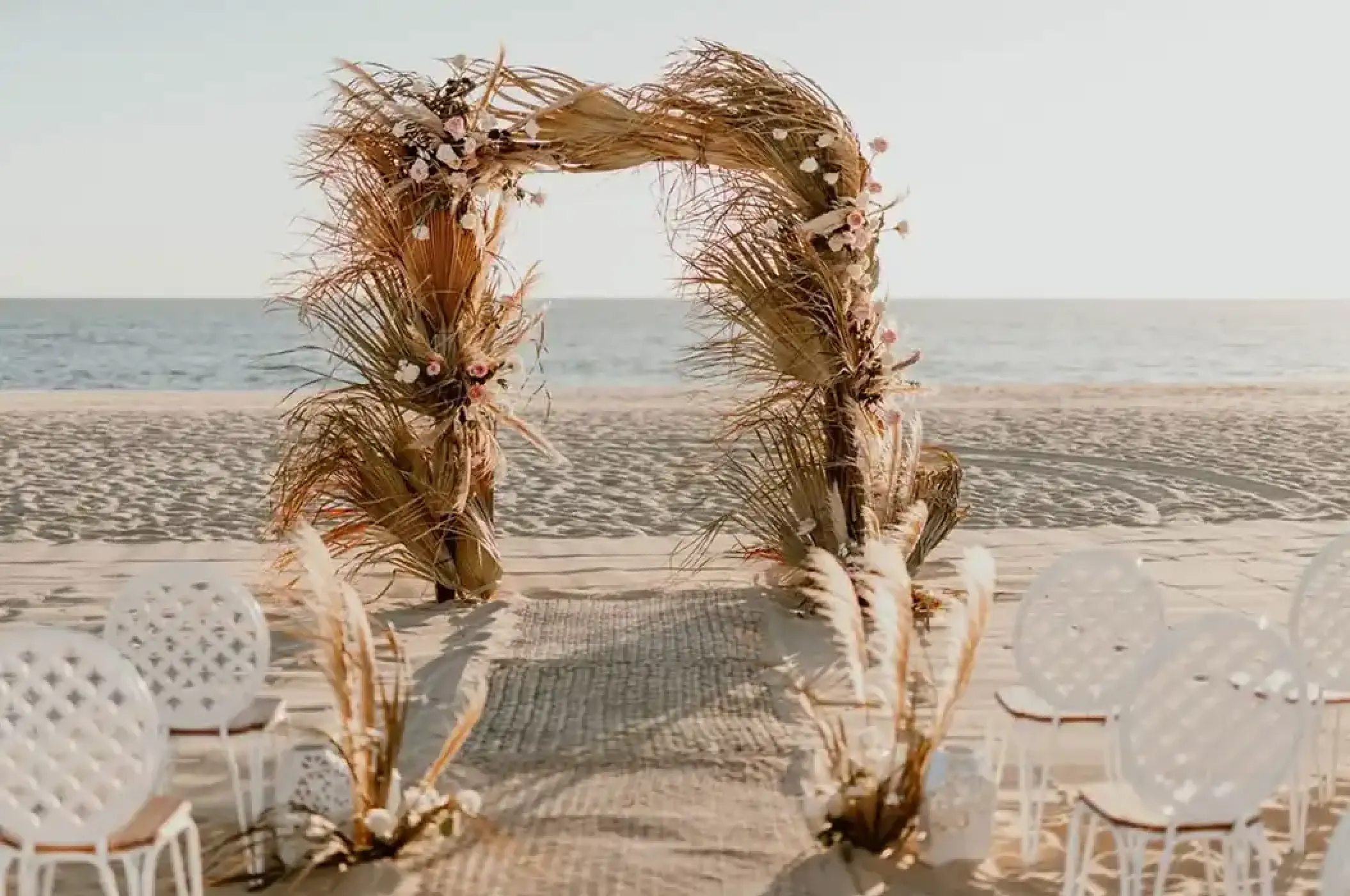 Beachfront wedding ceremony setup with a dried palm arch at Nobu Los Cabos, Cabo San Lucas