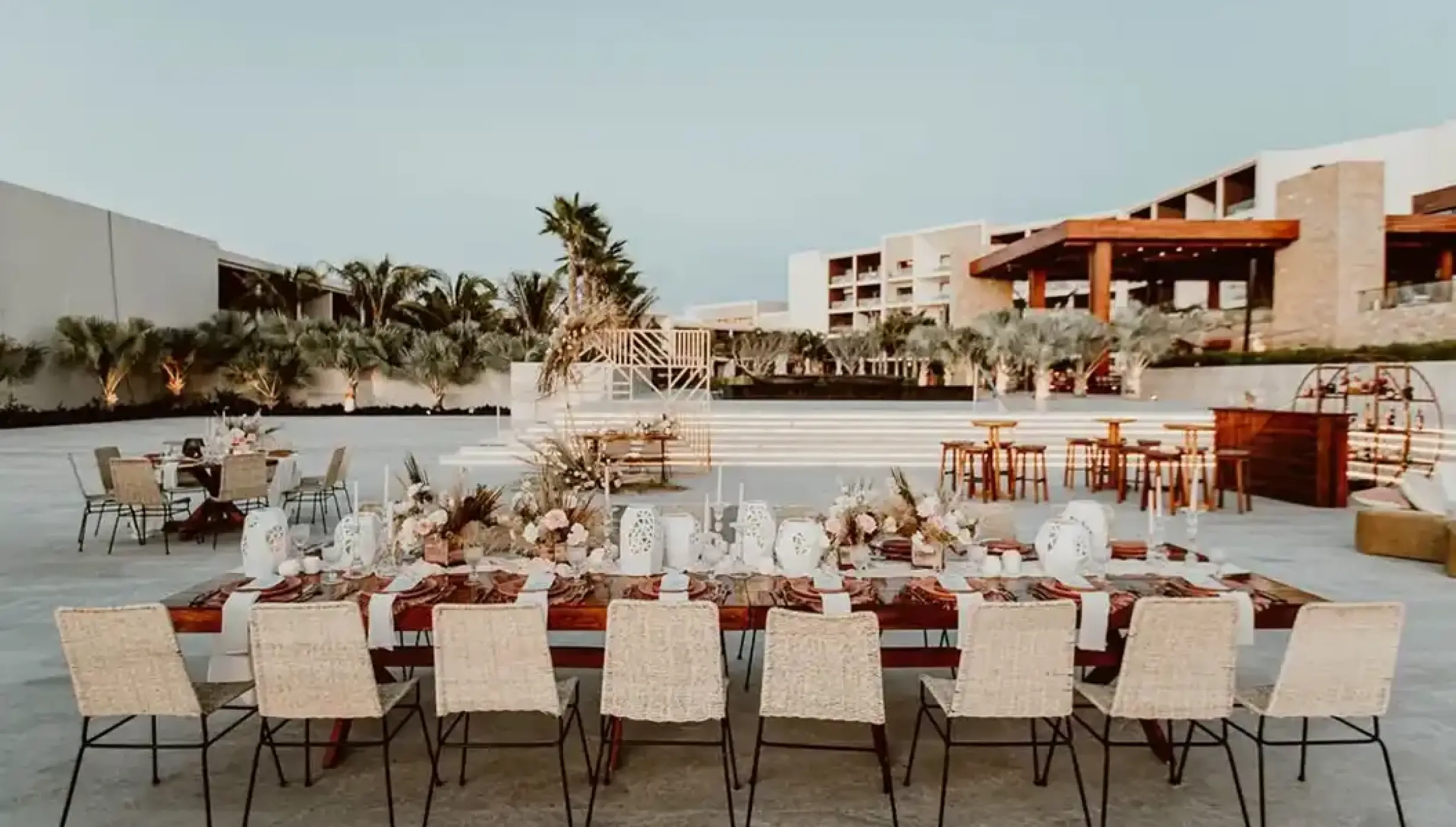 Outdoor wedding reception setup with wooden tables and woven chairs at Nobu Hotel Los Cabos, Cabo San Lucas