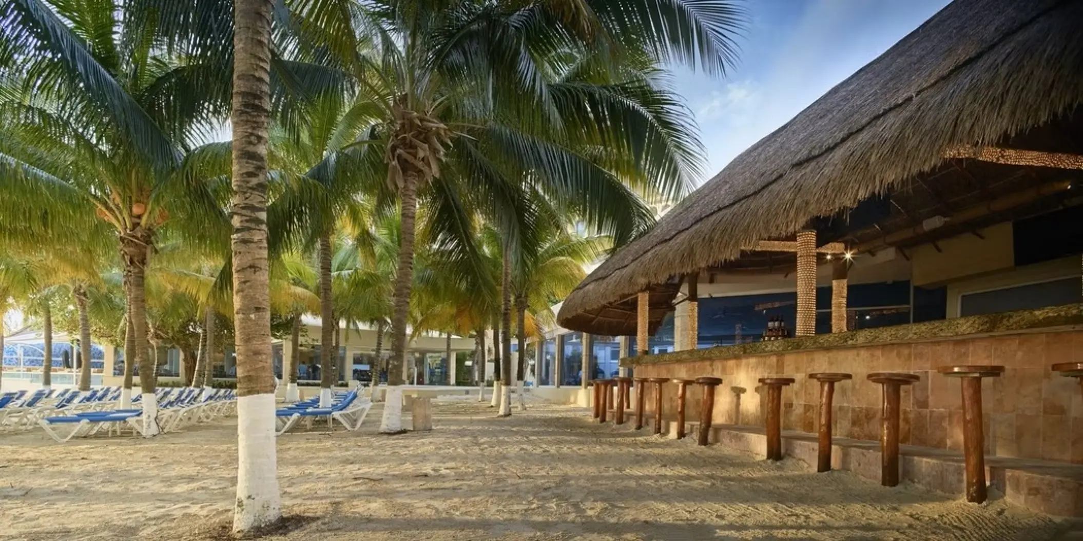Beachfront bar with a thatched roof and palm trees at Occidental Costa Cancun