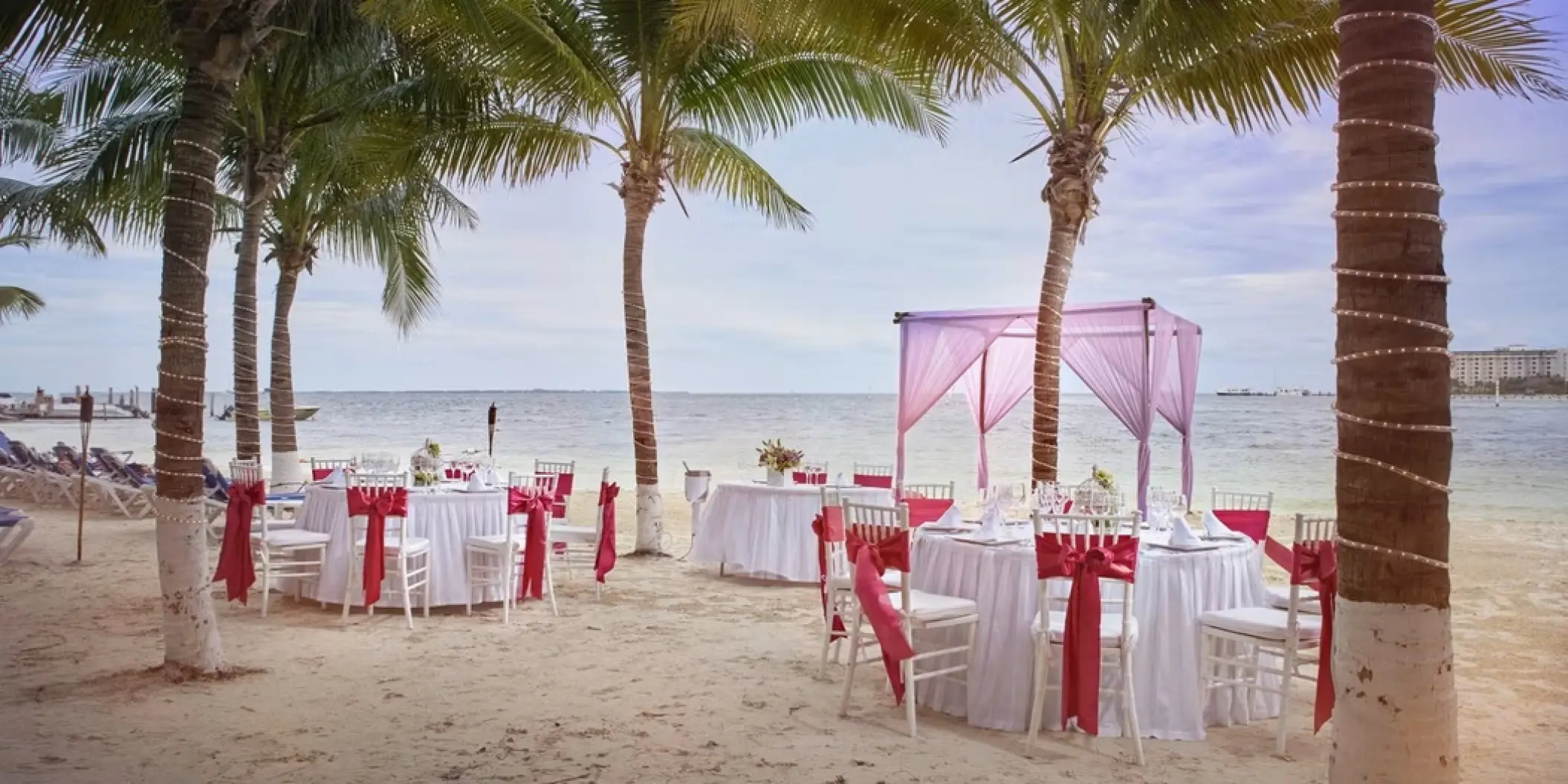 Beachfront wedding reception setup with pink canopy and red sashes at Occidental Costa Cancun