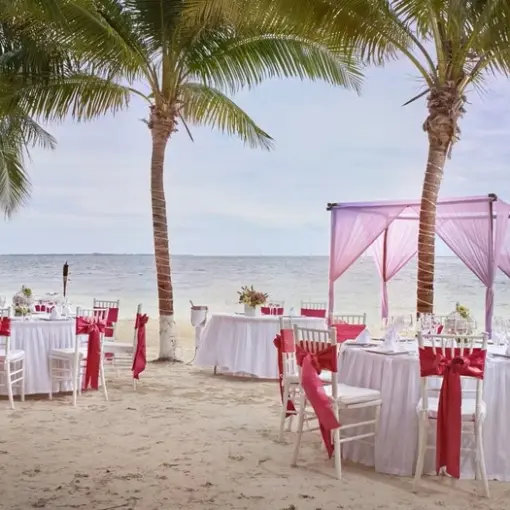 Beachfront wedding reception setup with pink canopy and red sashes at Occidental Costa Cancun