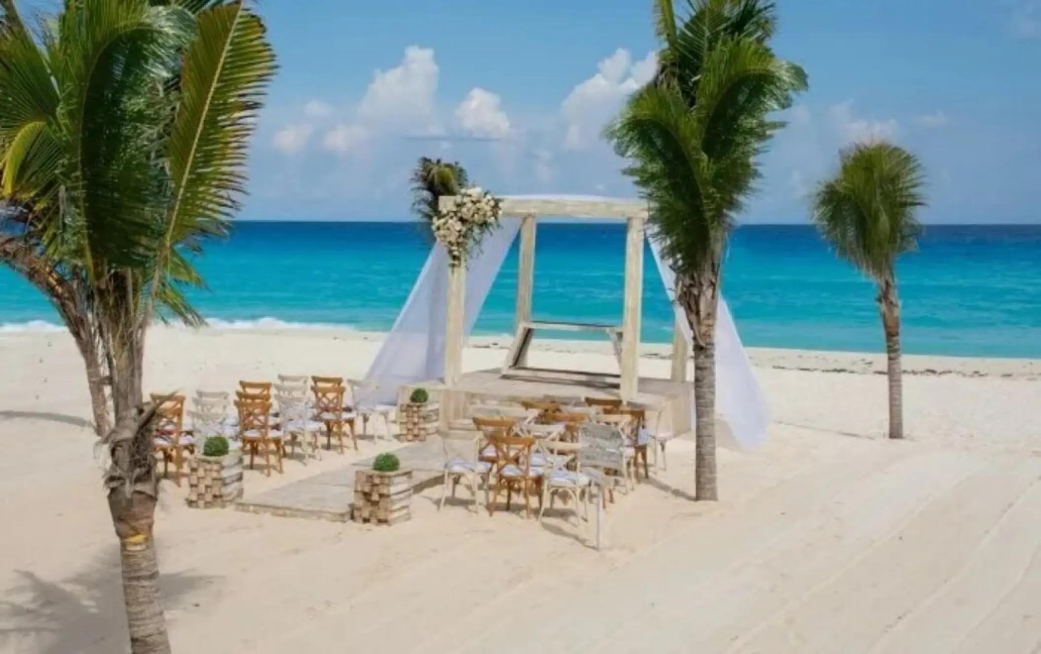 Beachfront wedding ceremony with a white gazebo and wooden chairs at Occidental Costa Cancun, Cancun