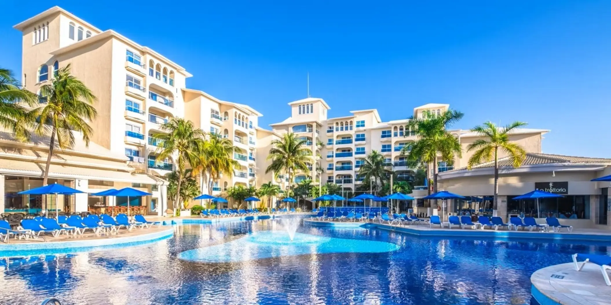 Large swimming pool with fountains surrounded by lounge chairs and blue umbrellas at Occidental Costa Cancun