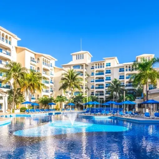 Large swimming pool with fountains surrounded by lounge chairs and blue umbrellas at Occidental Costa Cancun