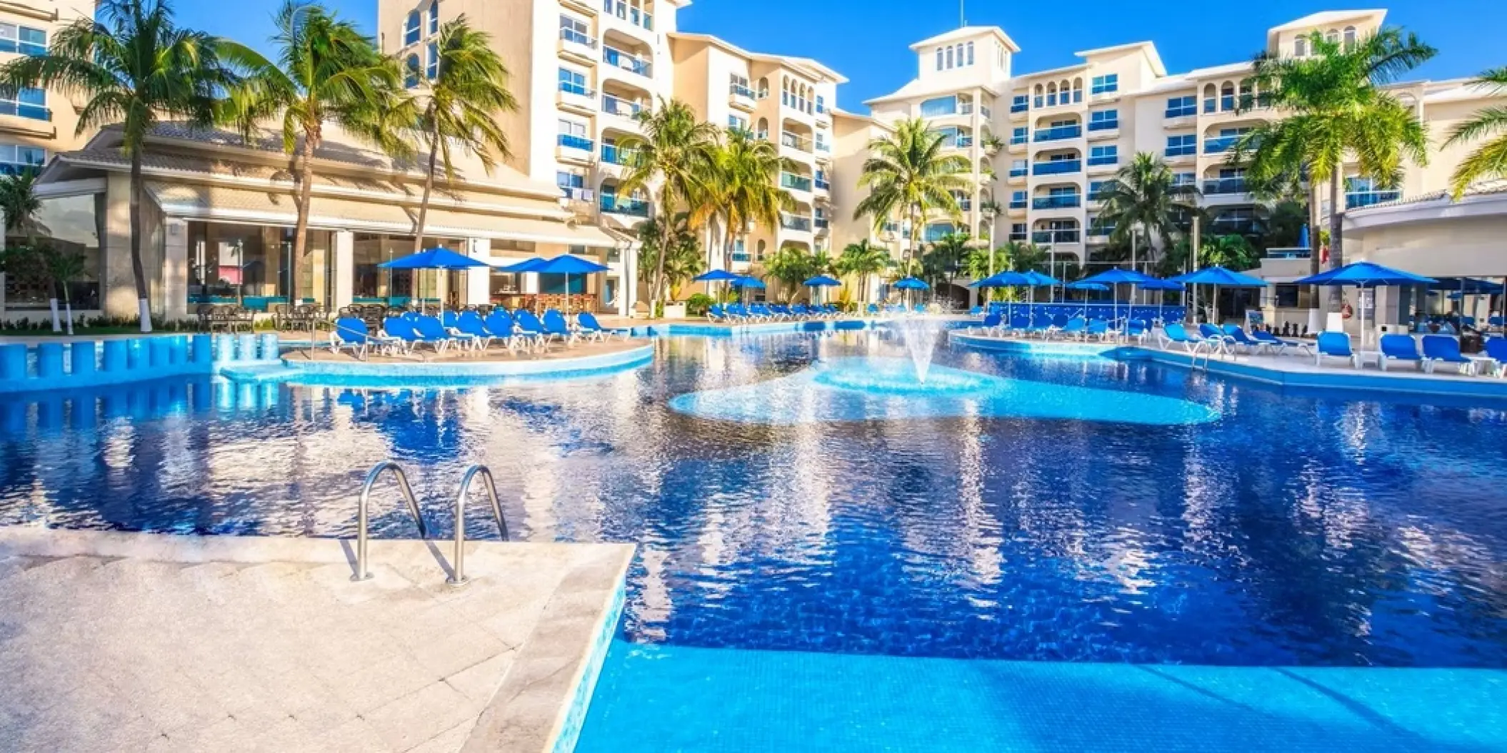 Large blue swimming pool with fountain and sun loungers at Occidental Costa Cancun