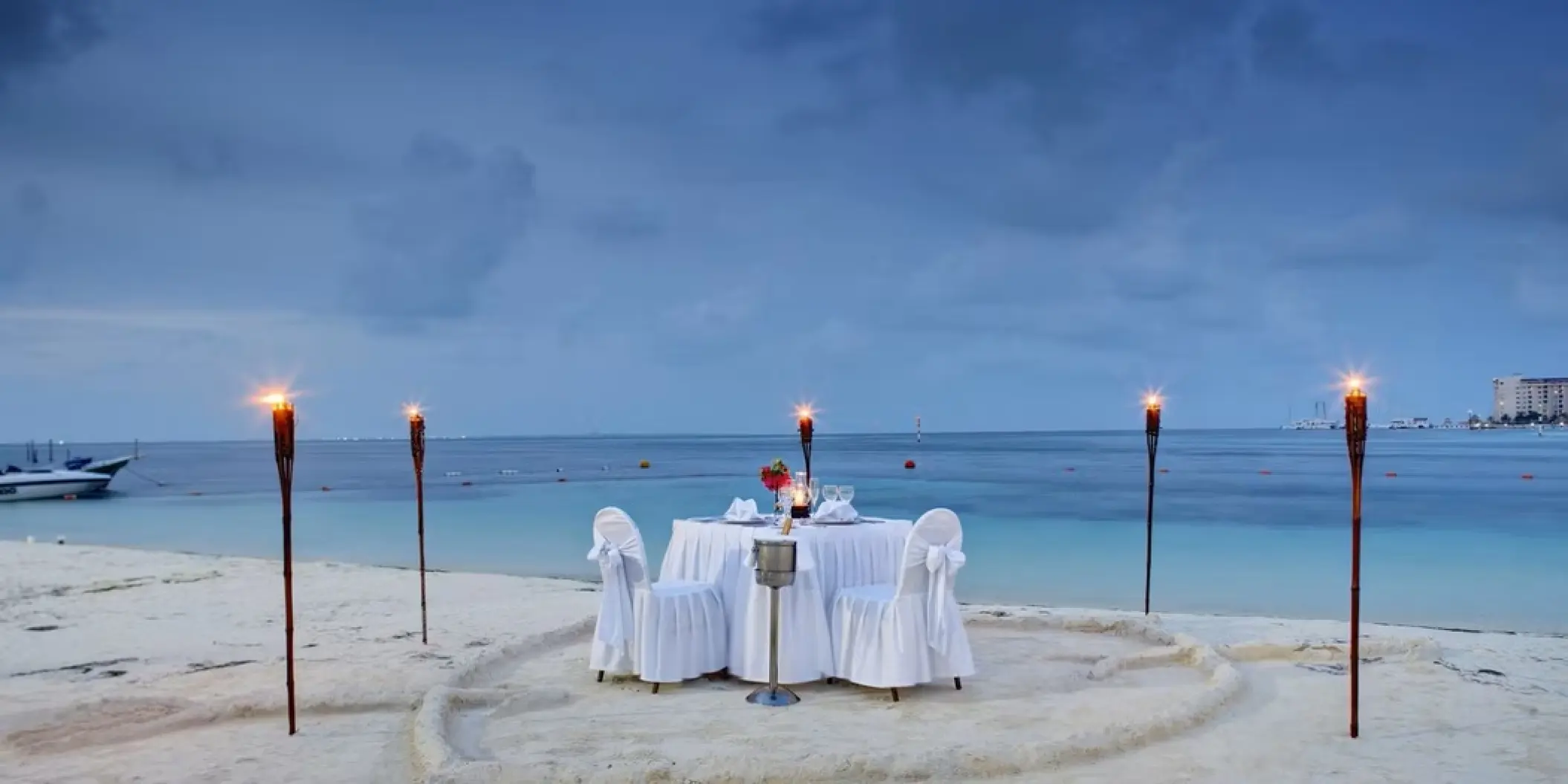 Private beach dinner setup with tiki torches and white linens at Occidental Costa Cancun