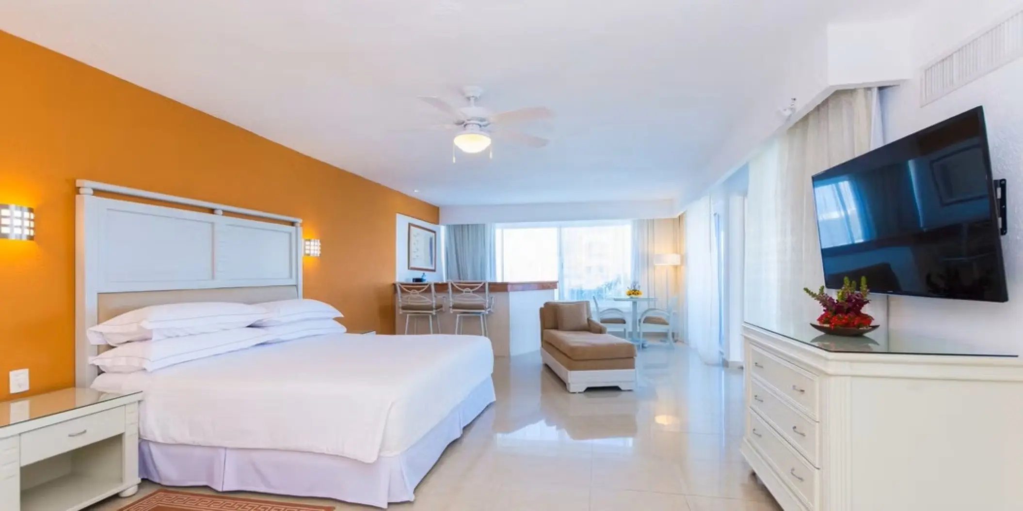 Modern guest suite with orange accent wall and white furnishings at Occidental Costa Cancun, Cancun