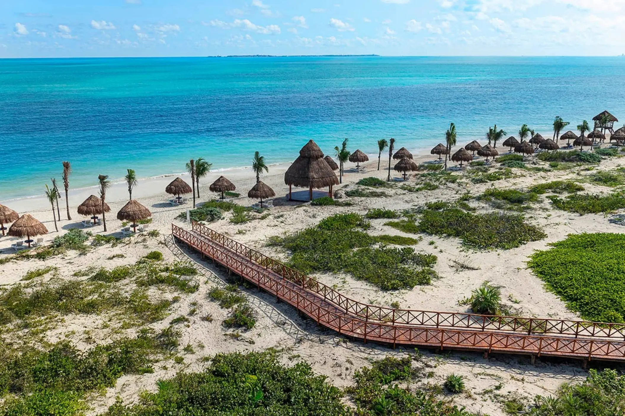 Wooden boardwalk leading to a white sand beach with palapas at Ocean Allure Costa Mujeres, Cancun