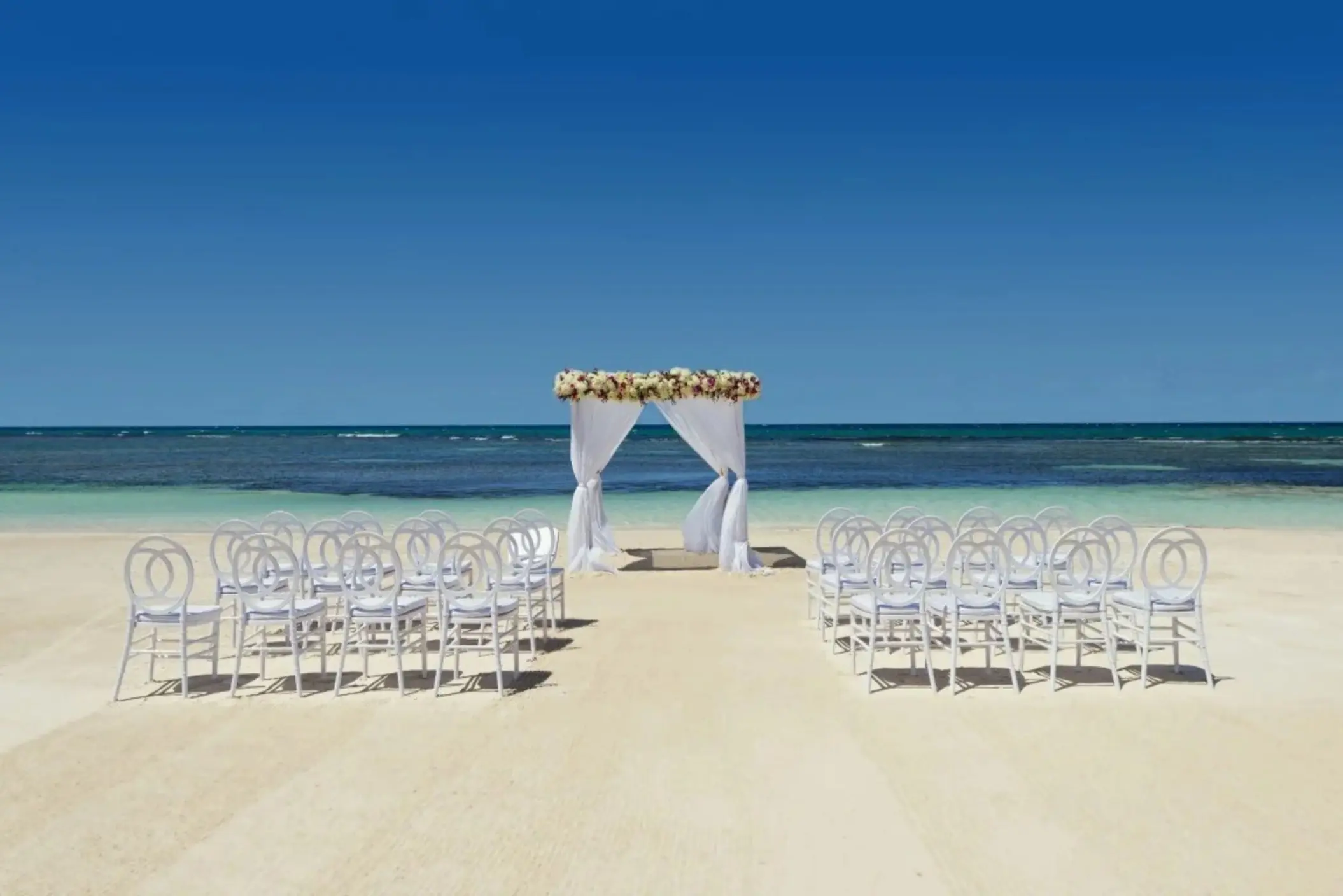 Beachfront wedding ceremony setup with white chairs and floral arch at Ocean Allure Costa Mujeres, Cancun