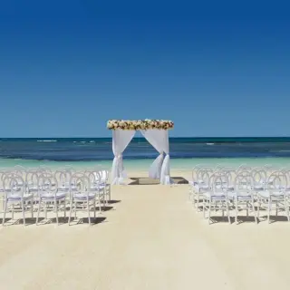 Beachfront wedding ceremony setup with white chairs and floral arch at Ocean Allure Costa Mujeres, Cancun