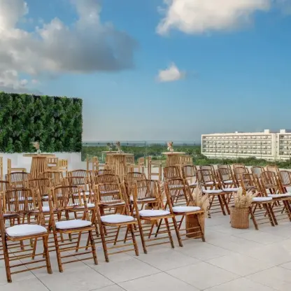 Rooftop wedding ceremony setup with wooden chairs and greenery wall at Ocean Allure Costa Mujeres, Cancun