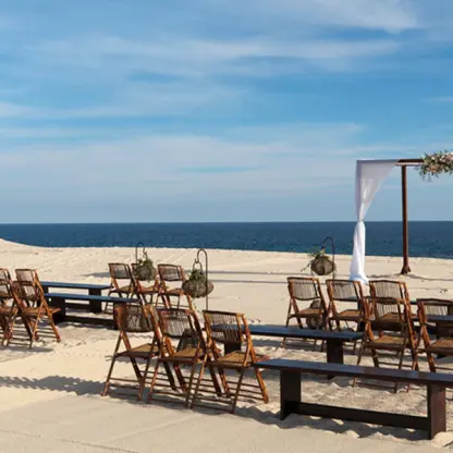 Beachfront wedding ceremony with wooden chairs and white fabric arch at Paradisus Los Cabos, Cabo San Lucas
