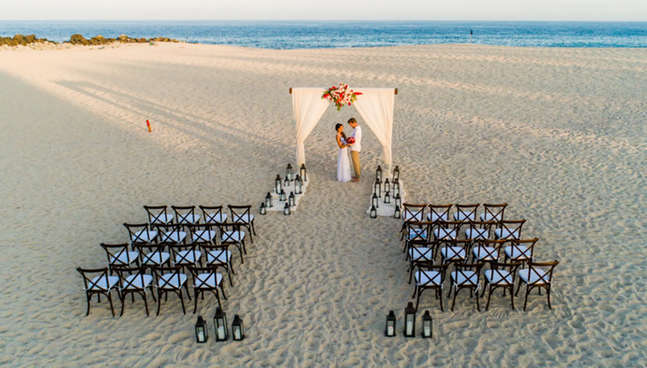 Beachfront wedding ceremony with draped arch and lantern aisle at Paradisus Los Cabos, Cabo San Lucas