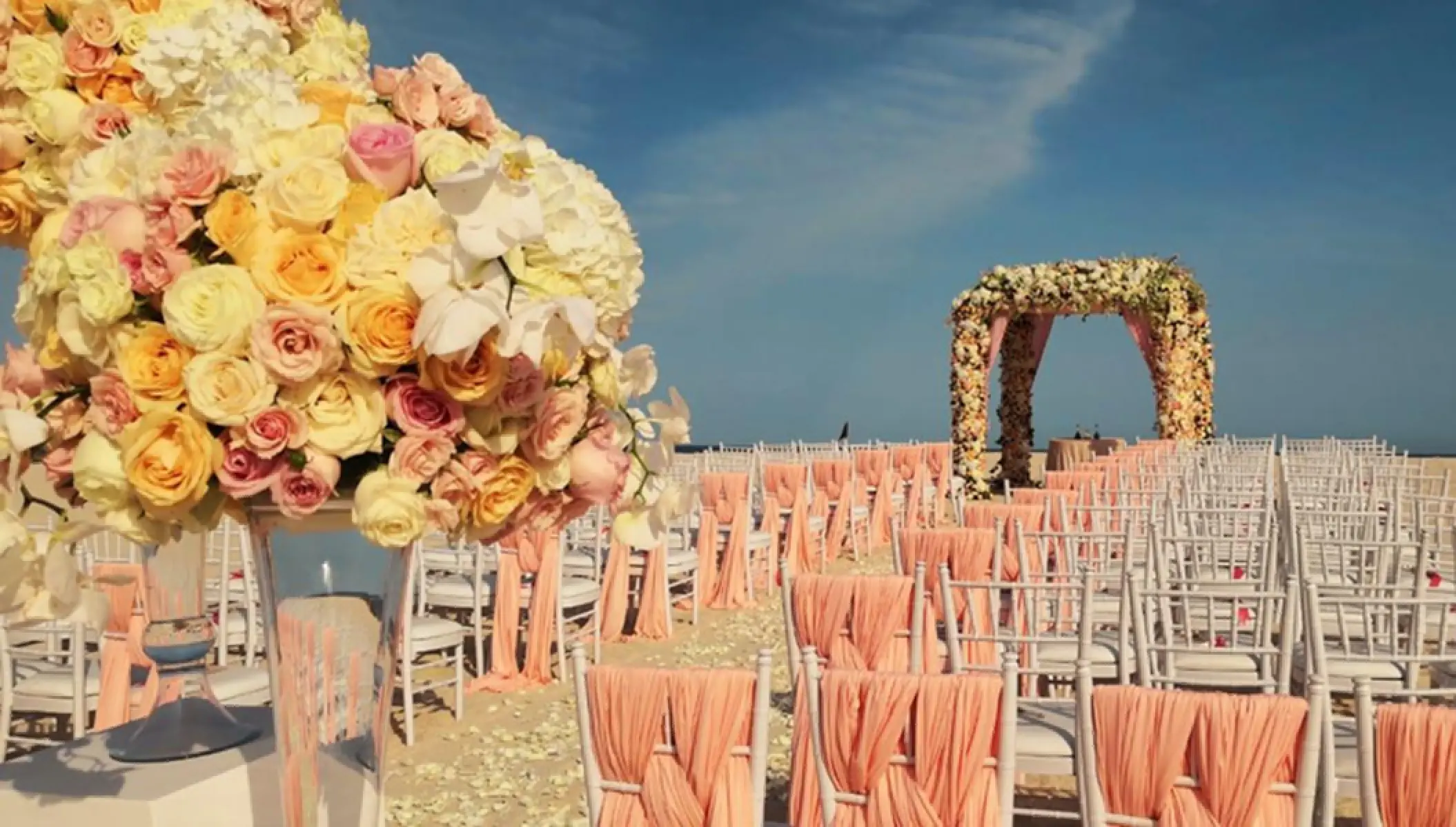 Beachfront wedding ceremony setup with floral arch and peach-draped chairs at Paradisus Los Cabos, Cabo San Lucas