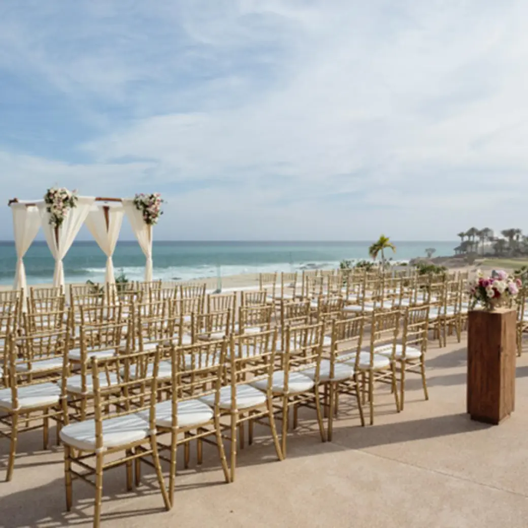 Ocean terrace wedding ceremony with gold chairs and white fabric arch at Paradisus Los Cabos, Cabo San Lucas