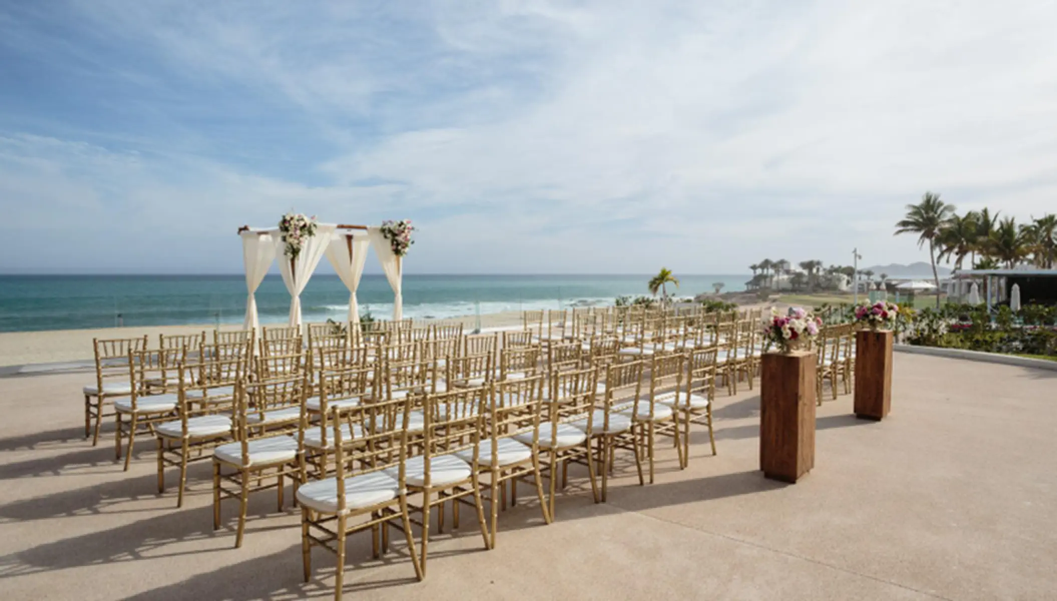 Ocean terrace wedding ceremony with gold chairs and white fabric arch at Paradisus Los Cabos, Cabo San Lucas