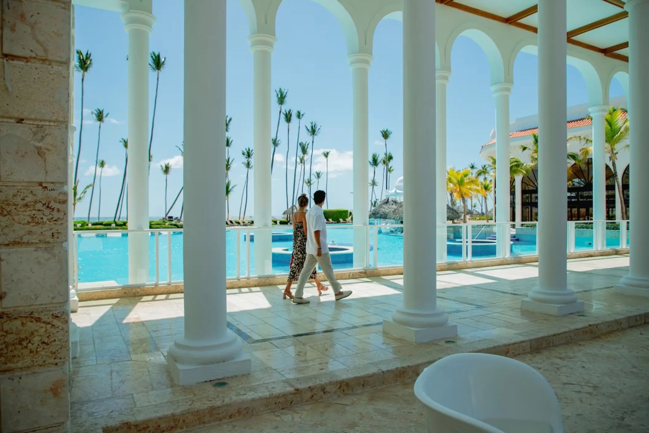 Couple walking through a white colonnade terrace at Paradisus Palma Real, Punta Cana
