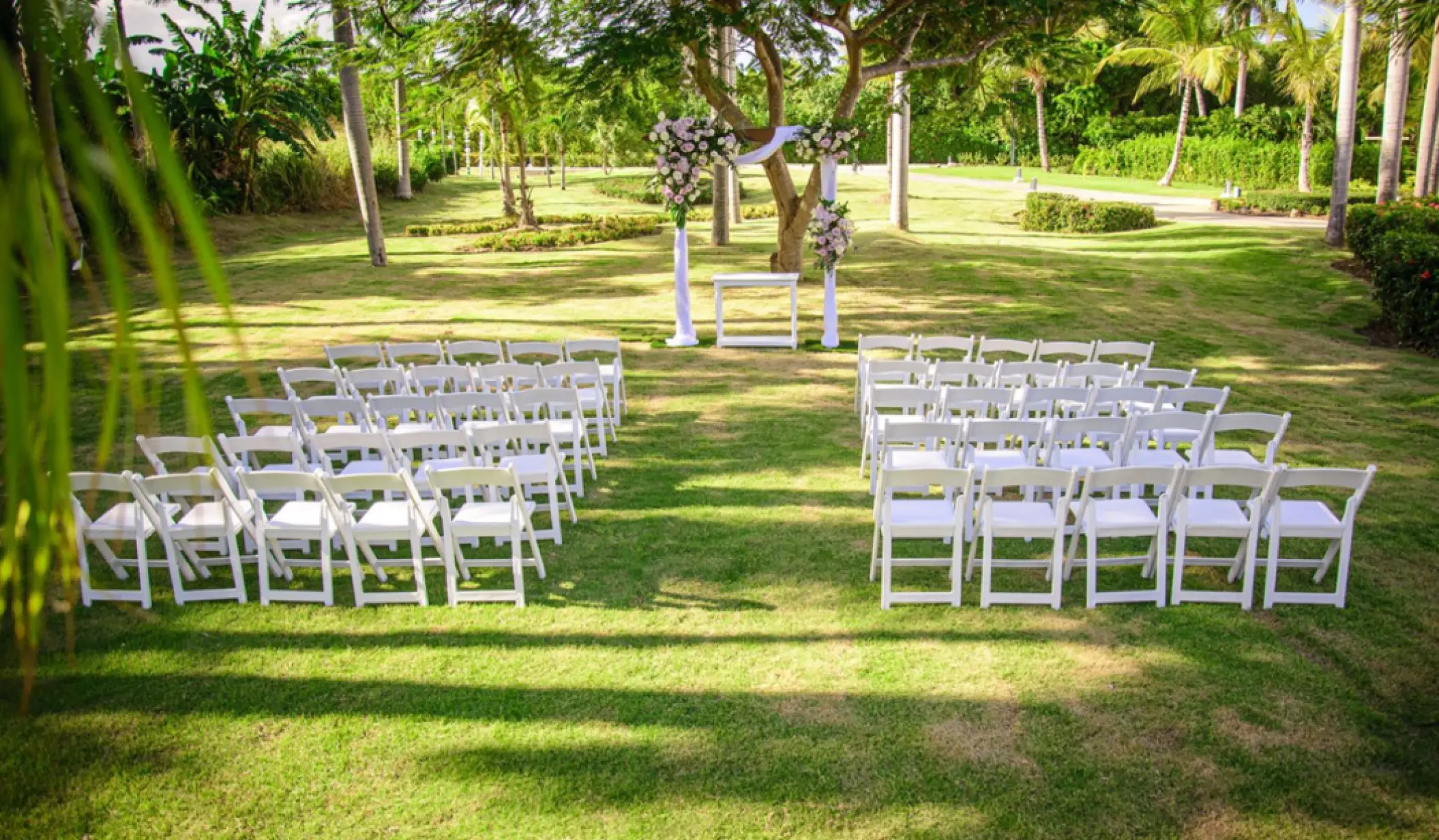 Garden wedding ceremony with white folding chairs and a floral arch at Paradisus Palma Real, Punta Cana