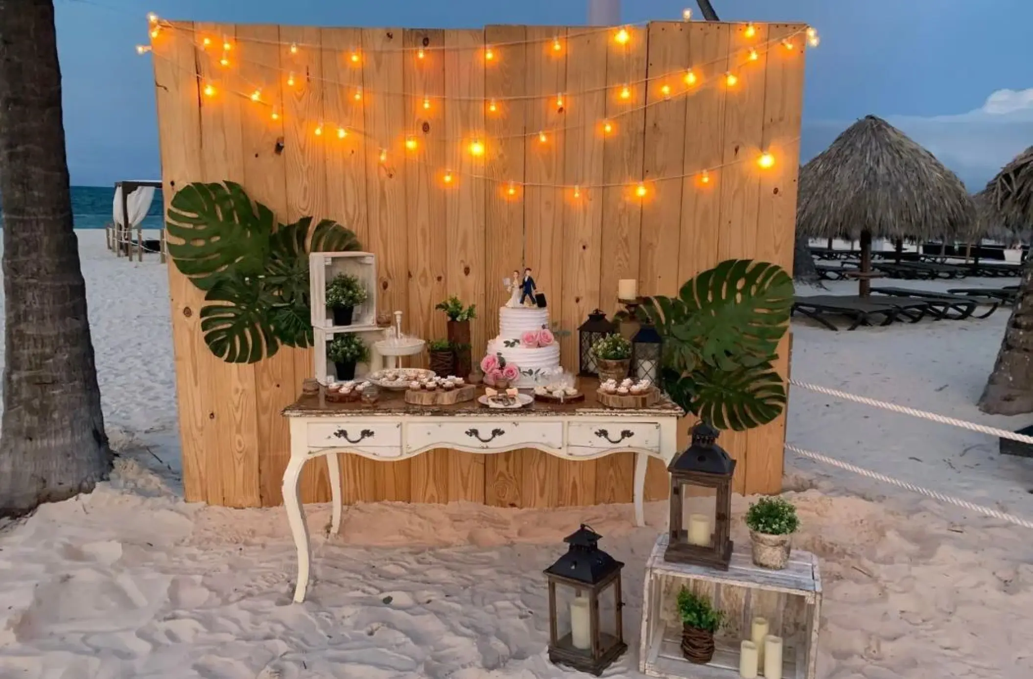 Rustic beach wedding cake table with string lights and tropical greenery at Paradisus Palma Real, Punta Cana