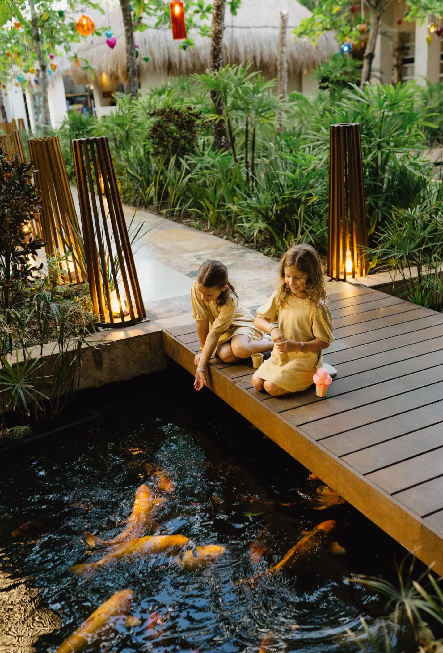 Two children feeding koi fish from a wooden walkway at Paradisus Playa Del Carmen