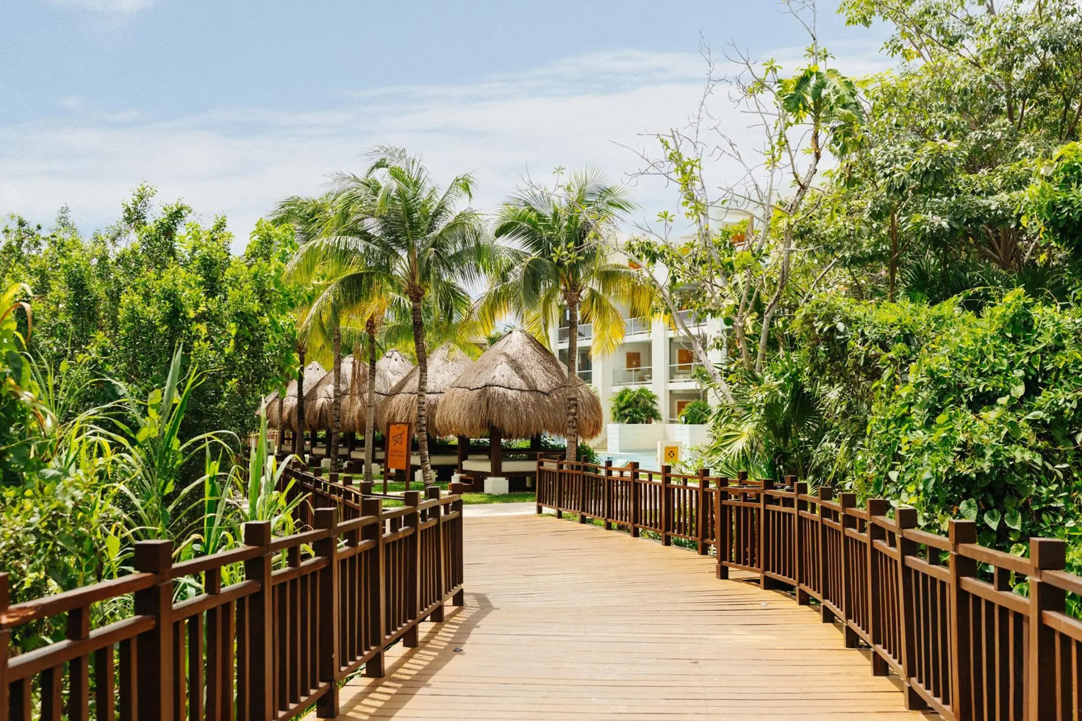 Wooden walkway leading past palm trees and thatched palapas at Paradisus Playa Del Carmen