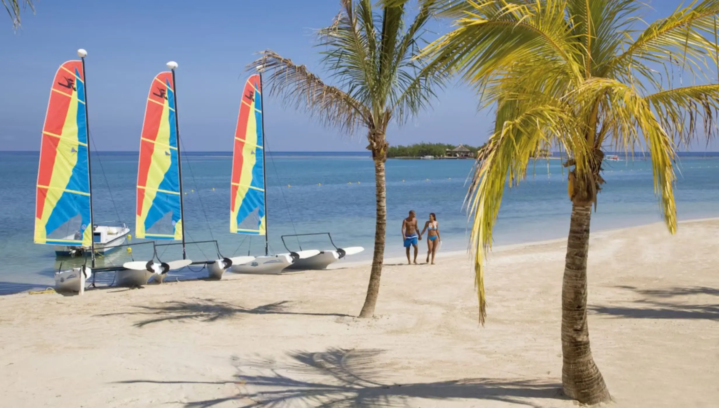 Couple walking on the beach by small sailboats at Riu Montego Bay, Montego Bay