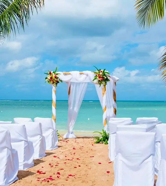 Beachfront wedding ceremony with a white draped arch and chairs at Riu Montego Bay, Montego Bay