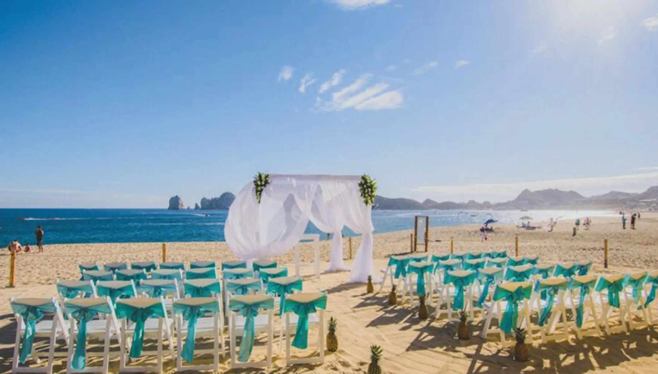 Beachfront wedding ceremony with turquoise sashes and white arch at Riu Palace Baja California, Cabo San Lucas
