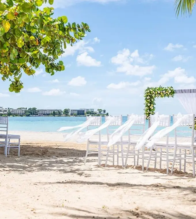 Beachfront wedding ceremony with white chairs and floral arch at Riu Palace Tropical Bay, Negril