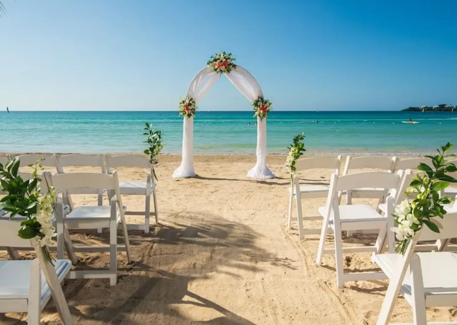 Beachfront wedding ceremony with a white fabric arch and chairs at Riu Palace Tropical Bay, Negril