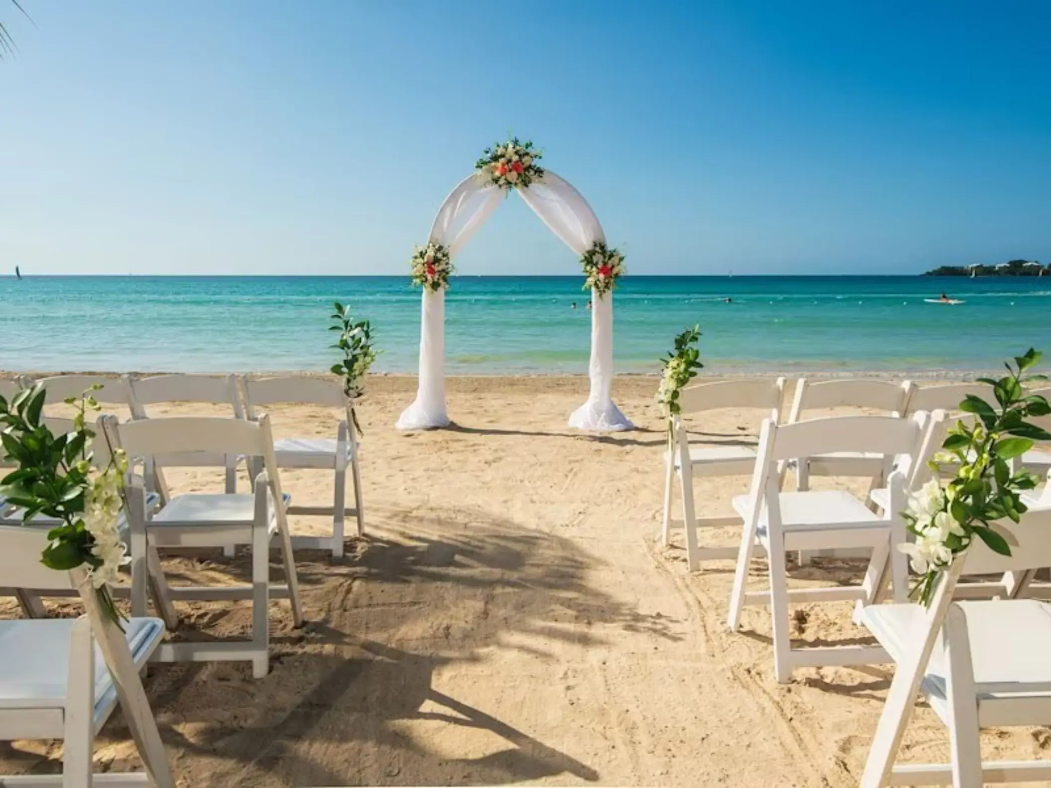 Beachfront wedding ceremony with a white fabric arch and chairs at Riu Palace Tropical Bay, Negril