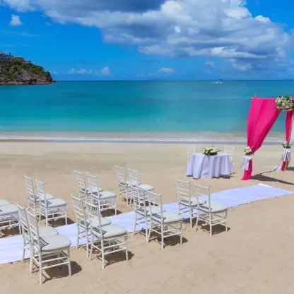 Beach wedding ceremony with pink draped arch and white chairs at Royalton Antigua, Five Islands Village
