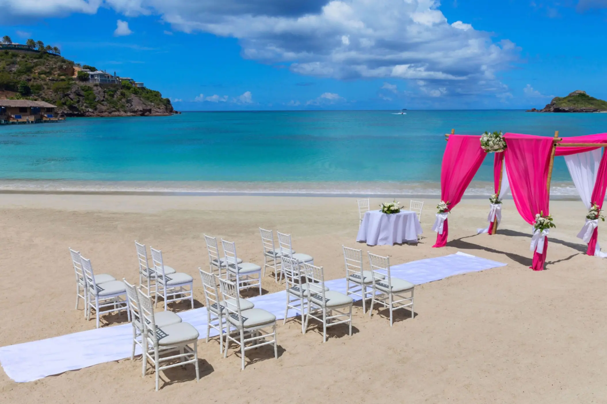 Beach wedding ceremony with pink draped arch and white chairs at Royalton Antigua, Five Islands Village