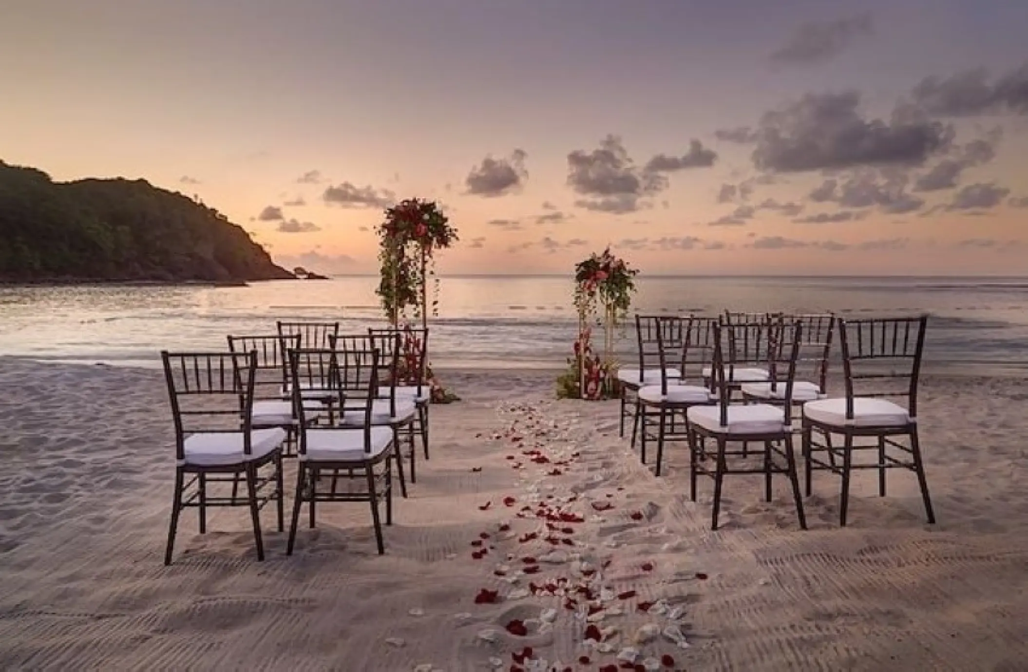 Beachfront wedding ceremony with rose petals and wooden chairs at Royalton Antigua, Five Islands Village