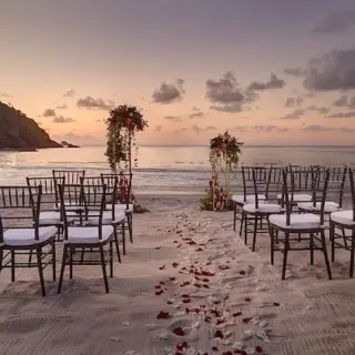 Beachfront wedding ceremony with rose petals and wooden chairs at Royalton Antigua, Five Islands Village