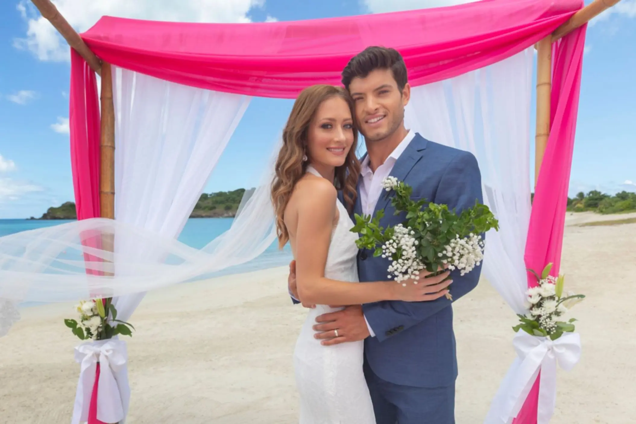 Bride and groom under a pink and white beach ceremony arch at Royalton Antigua, Five Islands Village