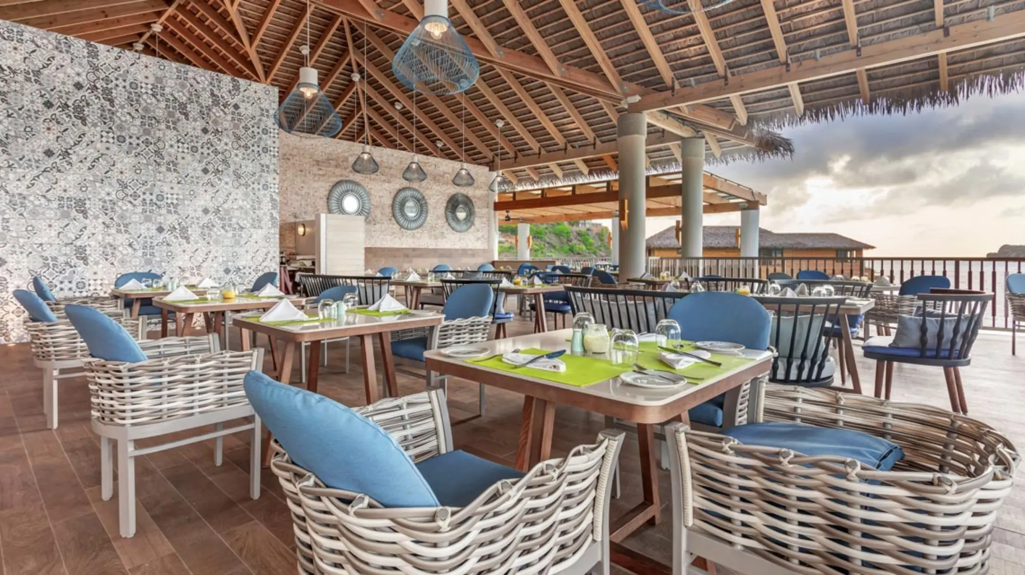 Outdoor restaurant with blue and white seating under a thatched roof at Royalton Antigua, Five Islands Village