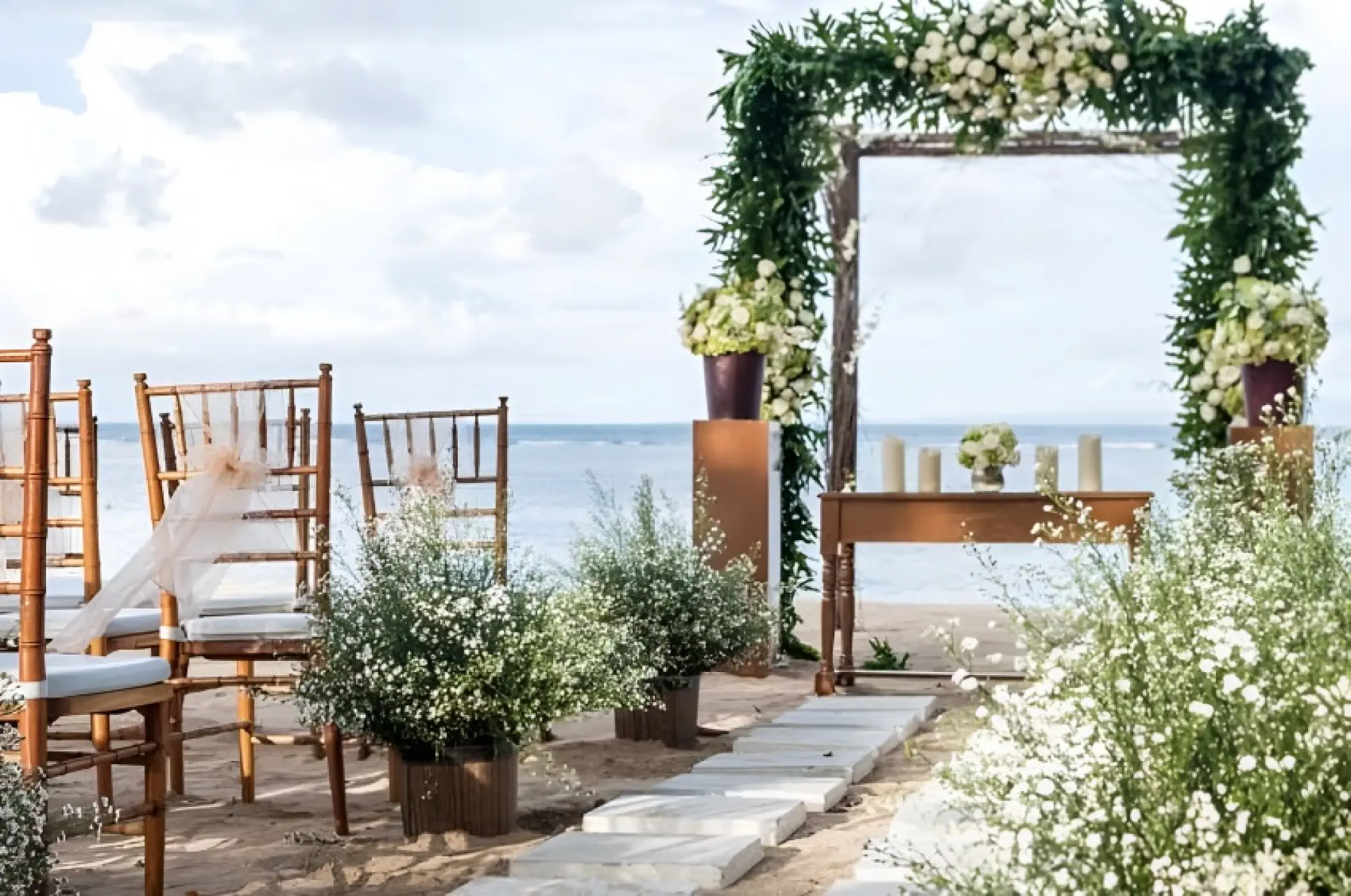 Beachfront wedding ceremony with a floral arch and wooden chairs at Royalton Antigua, Five Islands Village