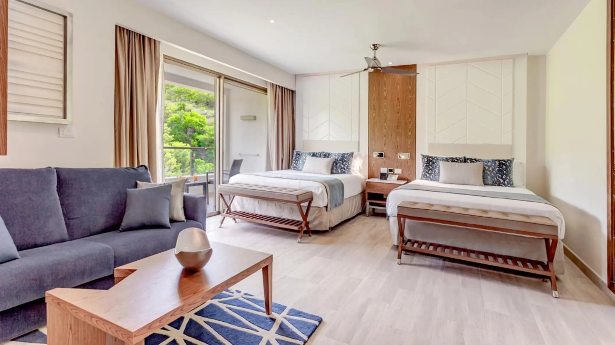 Modern suite with two beds and a blue sofa at Royalton Antigua, Five Islands Village