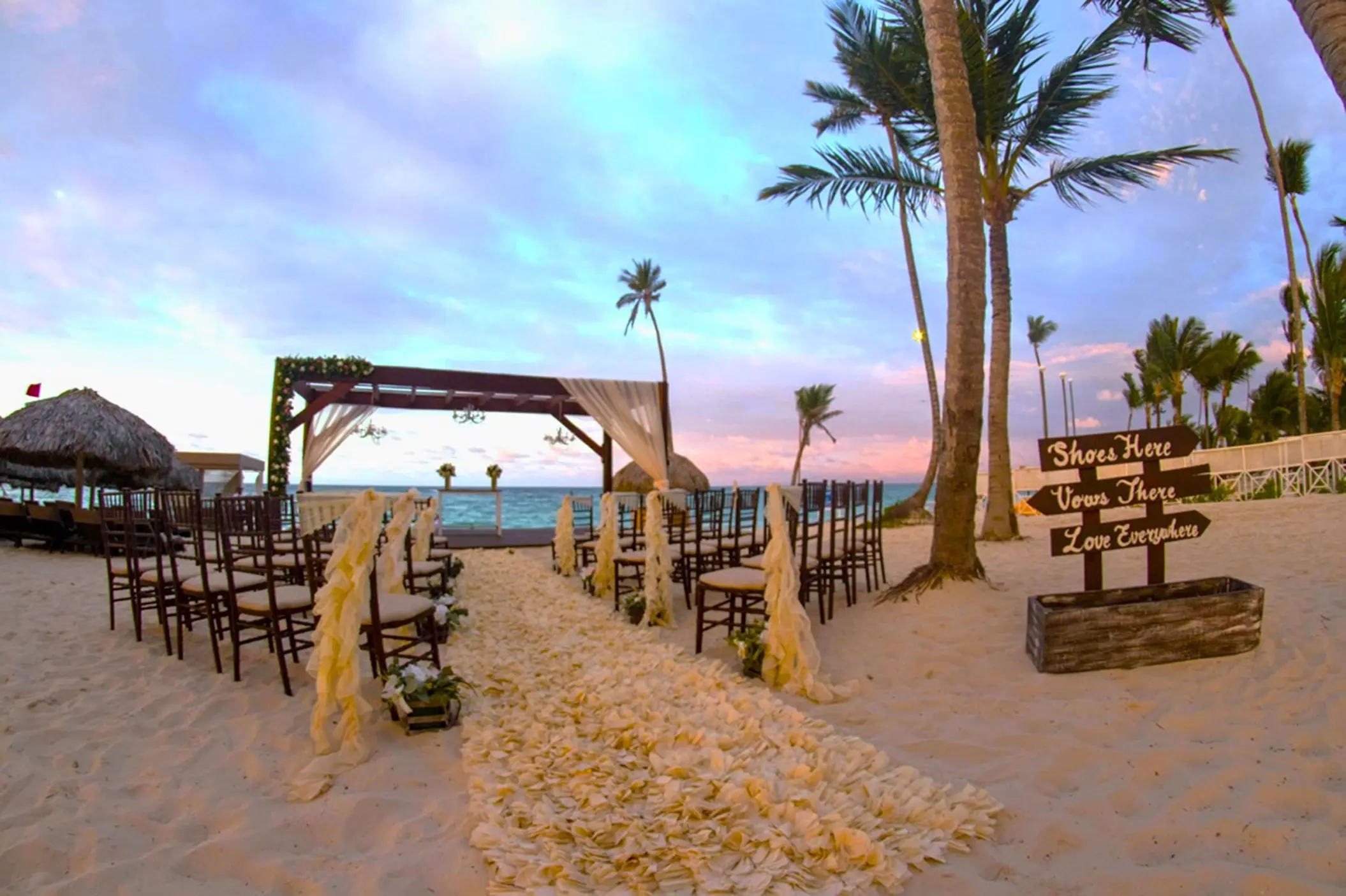 Beach wedding ceremony with a wooden arbor and floral aisle at Royalton Bavaro, Punta Cana