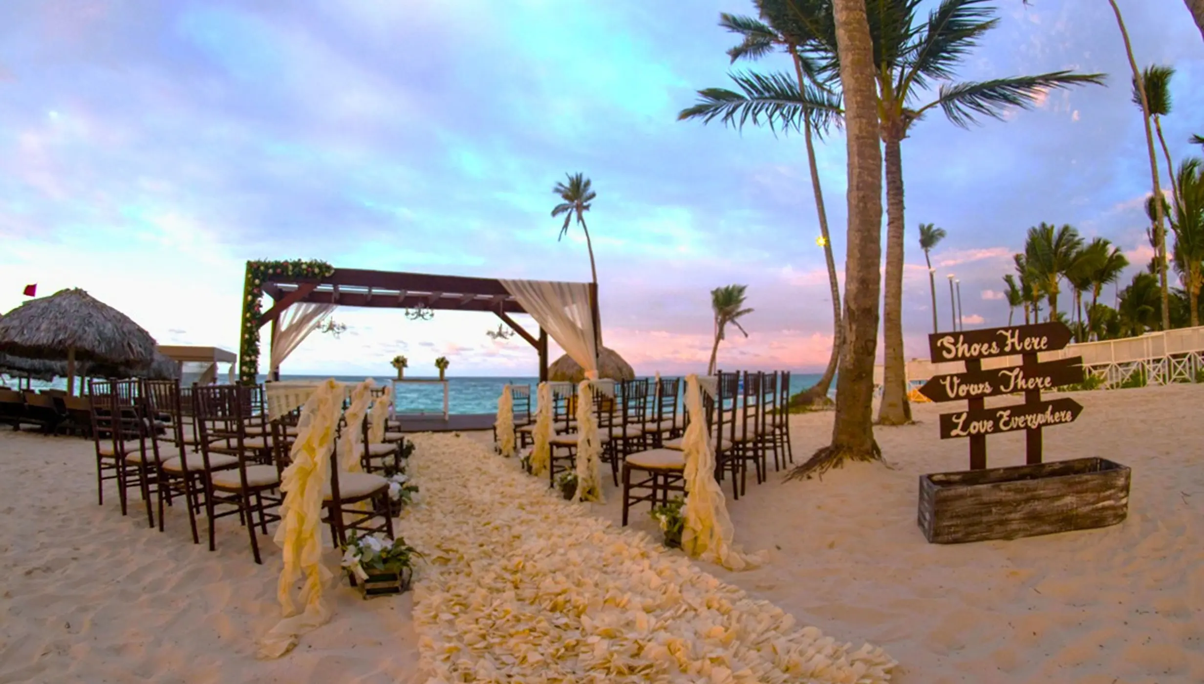 Beach wedding ceremony with a wooden arbor and floral aisle at Royalton Bavaro, Punta Cana