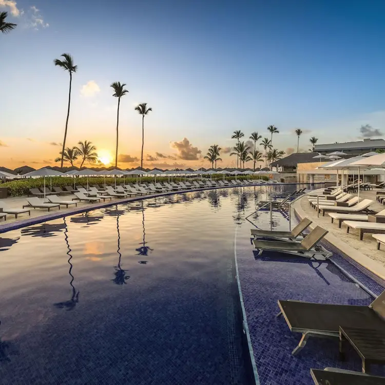 Long resort pool with lounge chairs and palm trees at sunset, Royalton Bavaro, Punta Cana