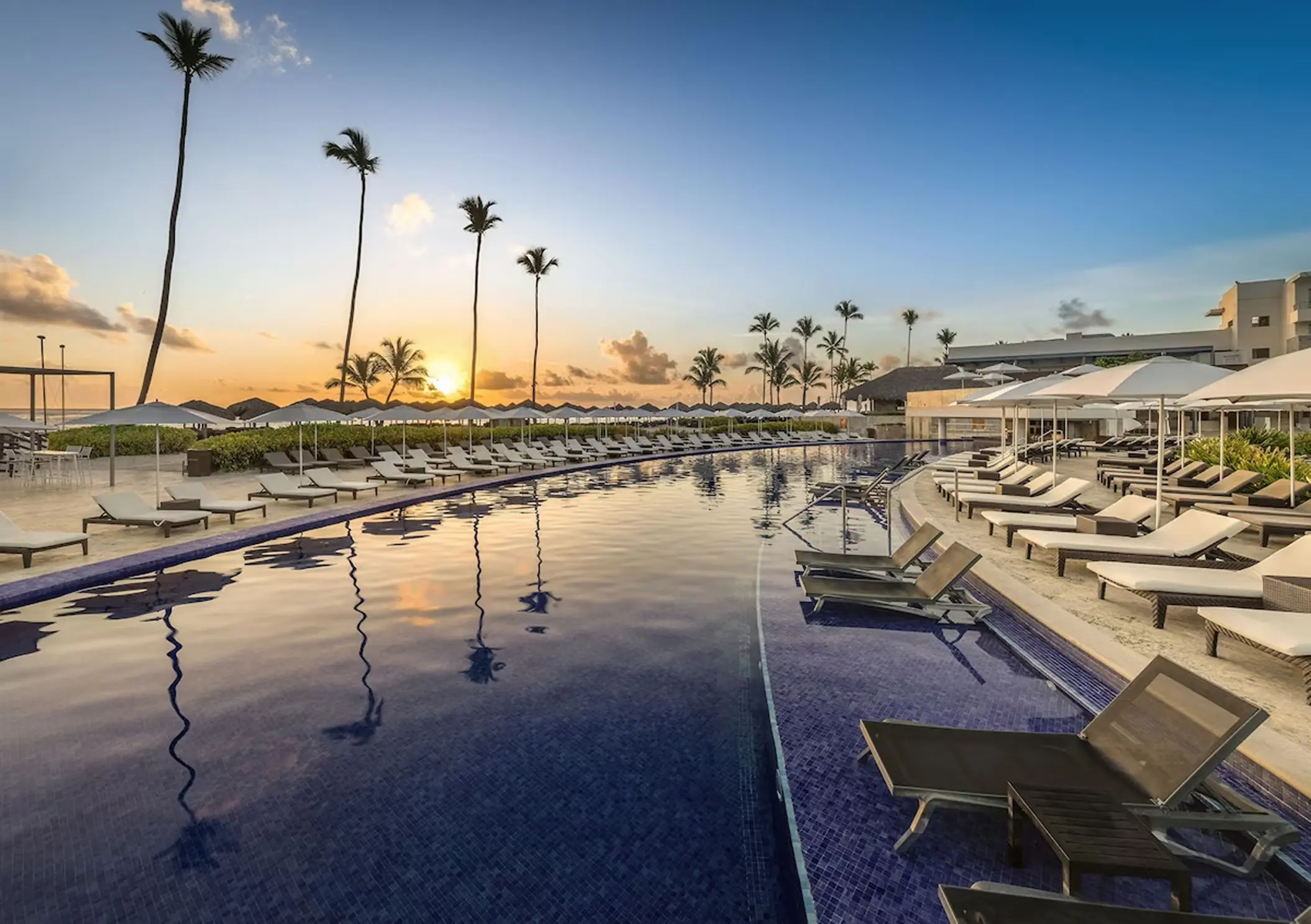 Long resort pool with lounge chairs and palm trees at sunset, Royalton Bavaro, Punta Cana