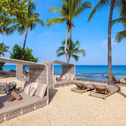 Woven beach cabanas and sun loungers under palm trees at Royalton Grenada, St. George’s