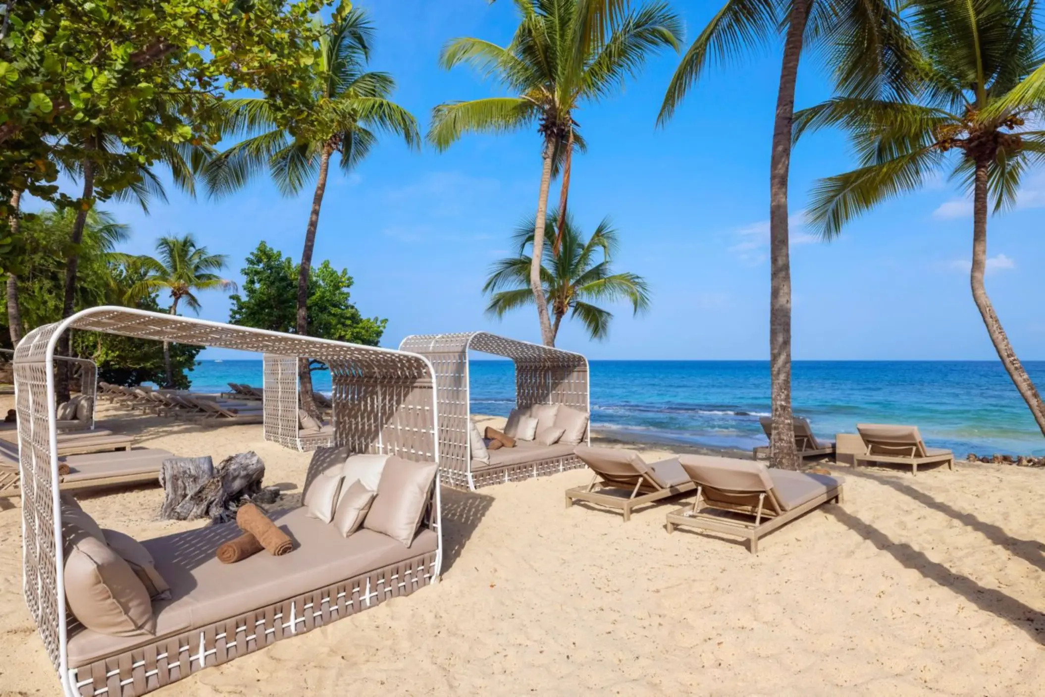 Woven beach cabanas and sun loungers under palm trees at Royalton Grenada, St. George’s