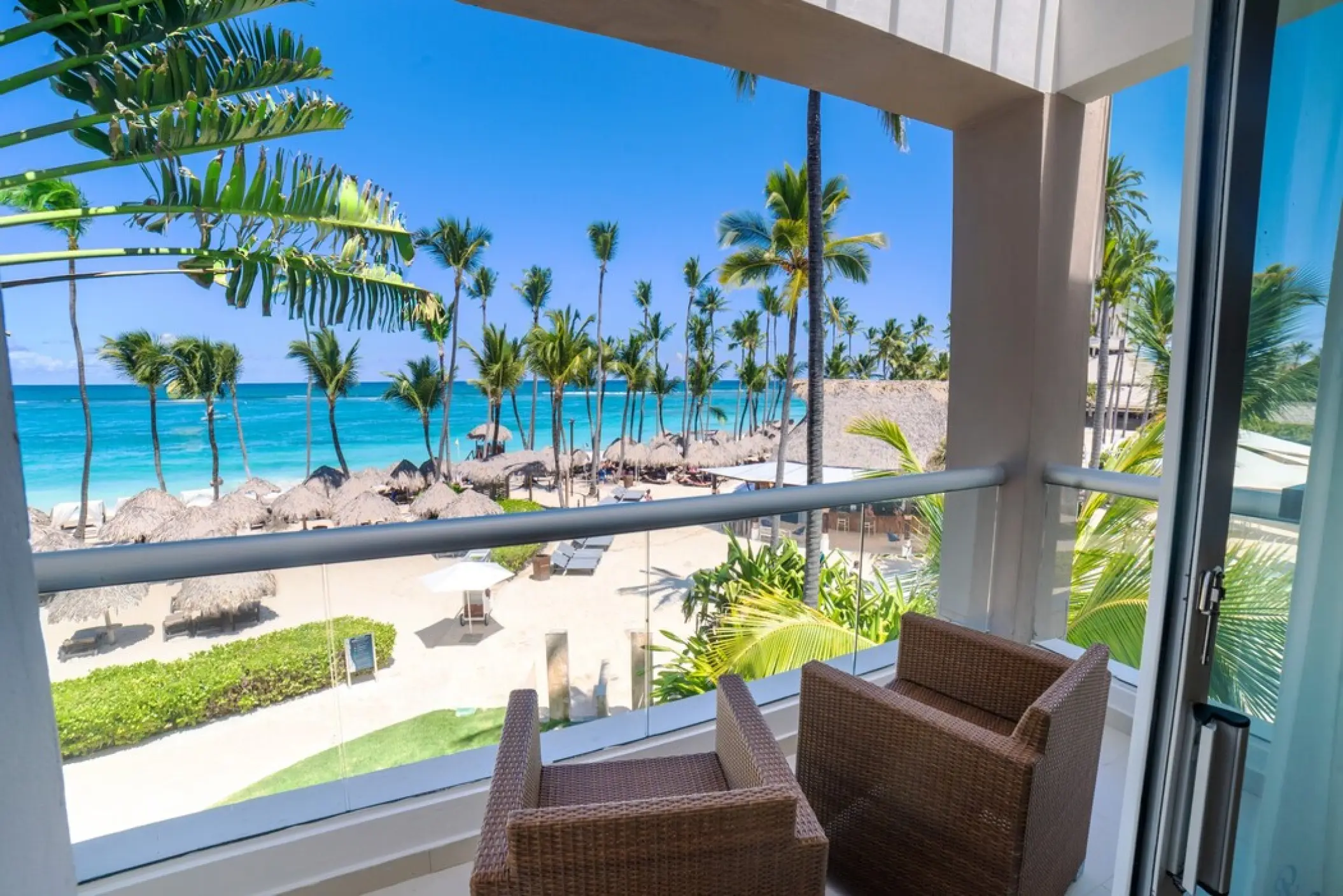 Suite balcony with wicker chairs overlooking the beach and palm trees at Royalton Punta Cana, Punta Cana